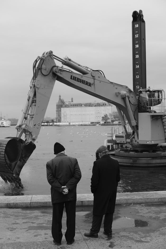 Two men observe a Liebherr excavator operating by the water, suggesting marine construction.